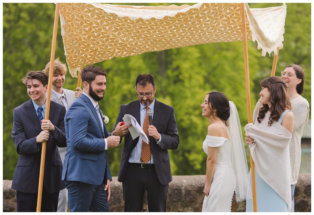 bride and groom laughing under the chuppah which is held by their siblings