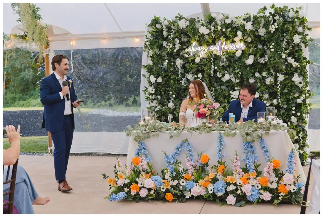best man gives wedding toast with bride and groom in front of floral installation that says always and forever