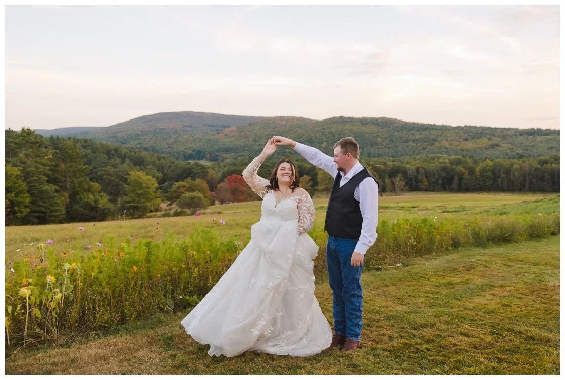 groom twirls bride while she holds her long train and smiles widely, golden hour with mountain backdrop