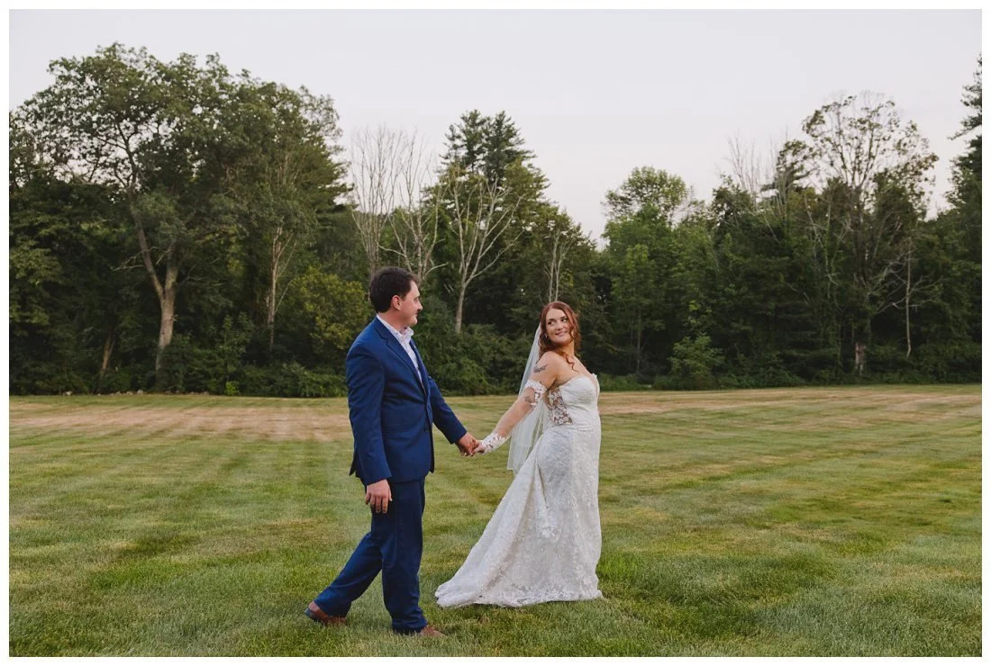 photo of bride leading groom on wide lawn with forest in the background