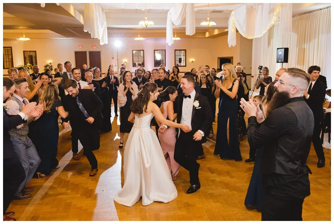 bride and groom in the center of the hora circle dancing while guests clap and cheer around them
