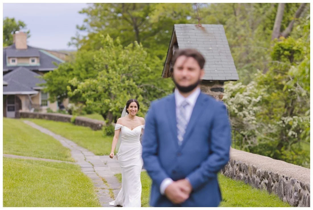 bride walks along path behind groom to surprise him for the first look