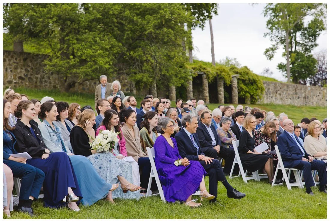 all the guests smiling and laughing during wedding ceremony on a grassy hillside
