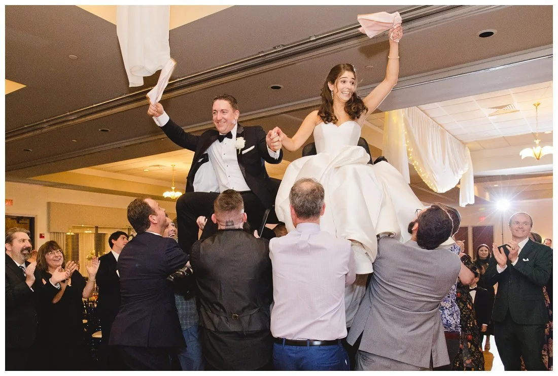 bride and groom get lifted on chairs during the hora and wave napkins around