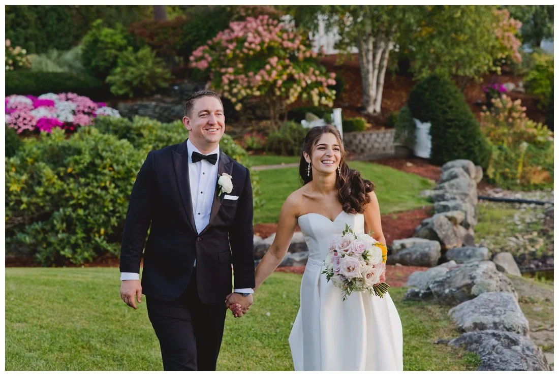 rachel and nick hold hands laughing with pink and white gardens behind them