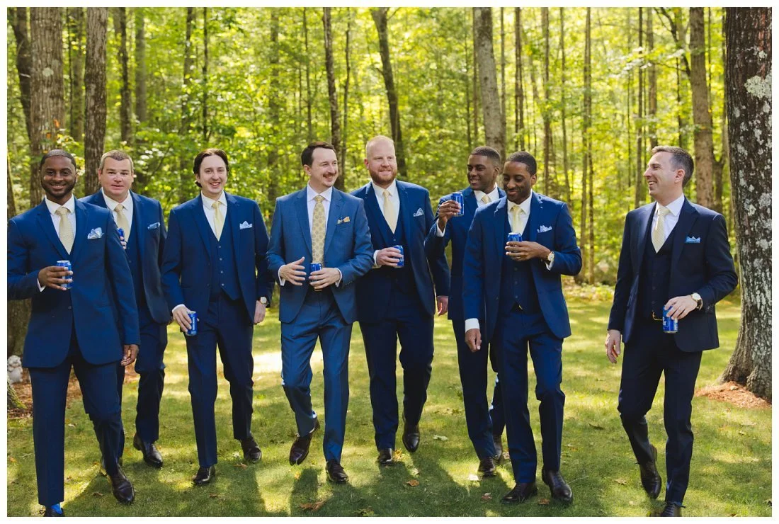 groom and his groomsmen in blue suits and yellow ties walking and drinking