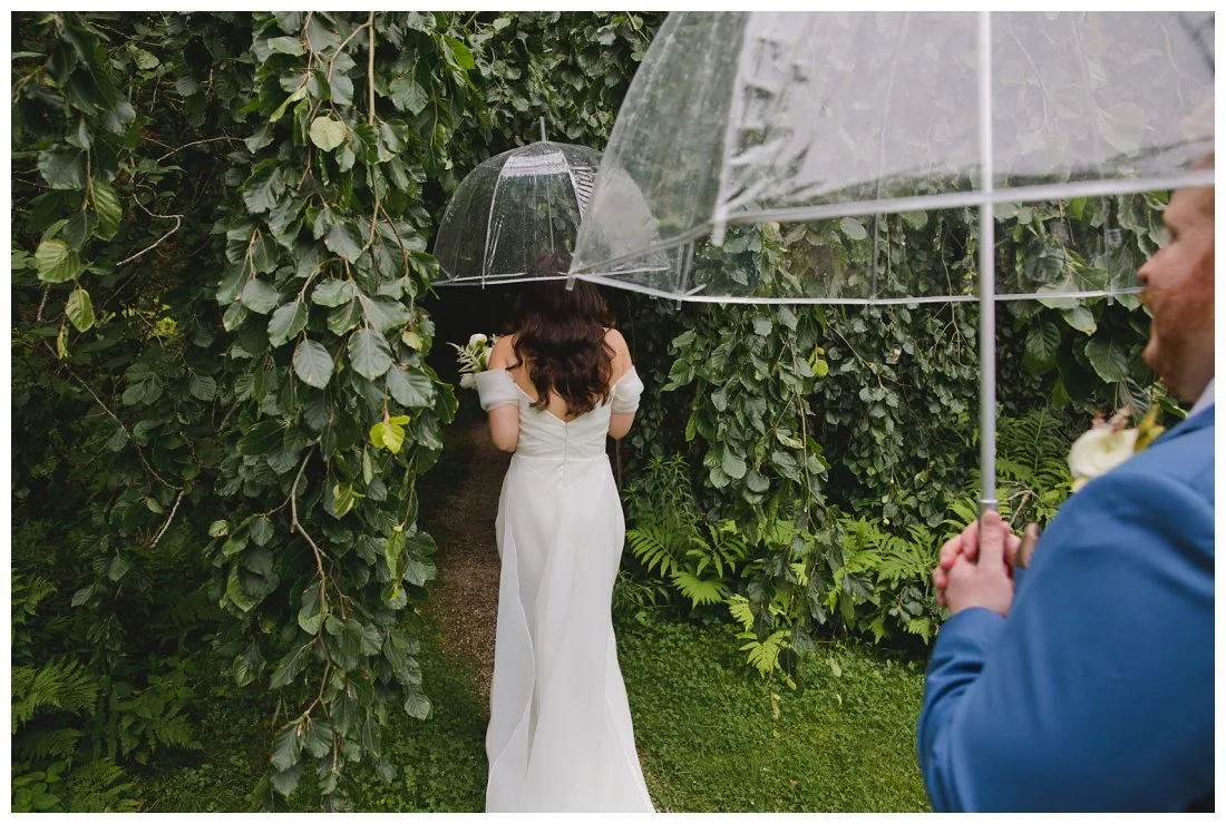 couples go under tree canopy holding clear umbrellas on rainy wedding day