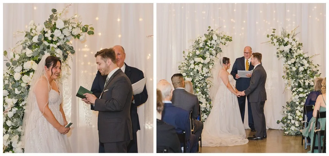 wedding ceremony with green and white flower arch as the focal point, flowy white curtains behind them with cafe lights shining through