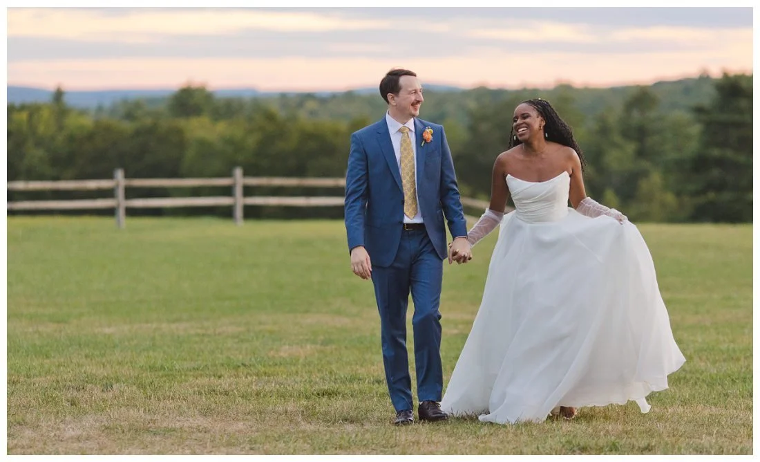 sunset wedding photos at dell lea, bride and groom walk through field with colorful sky behind them