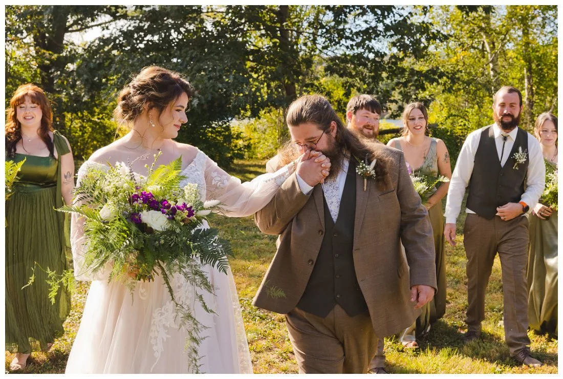 groom kisses bride's hand as they walk with their wedding party
