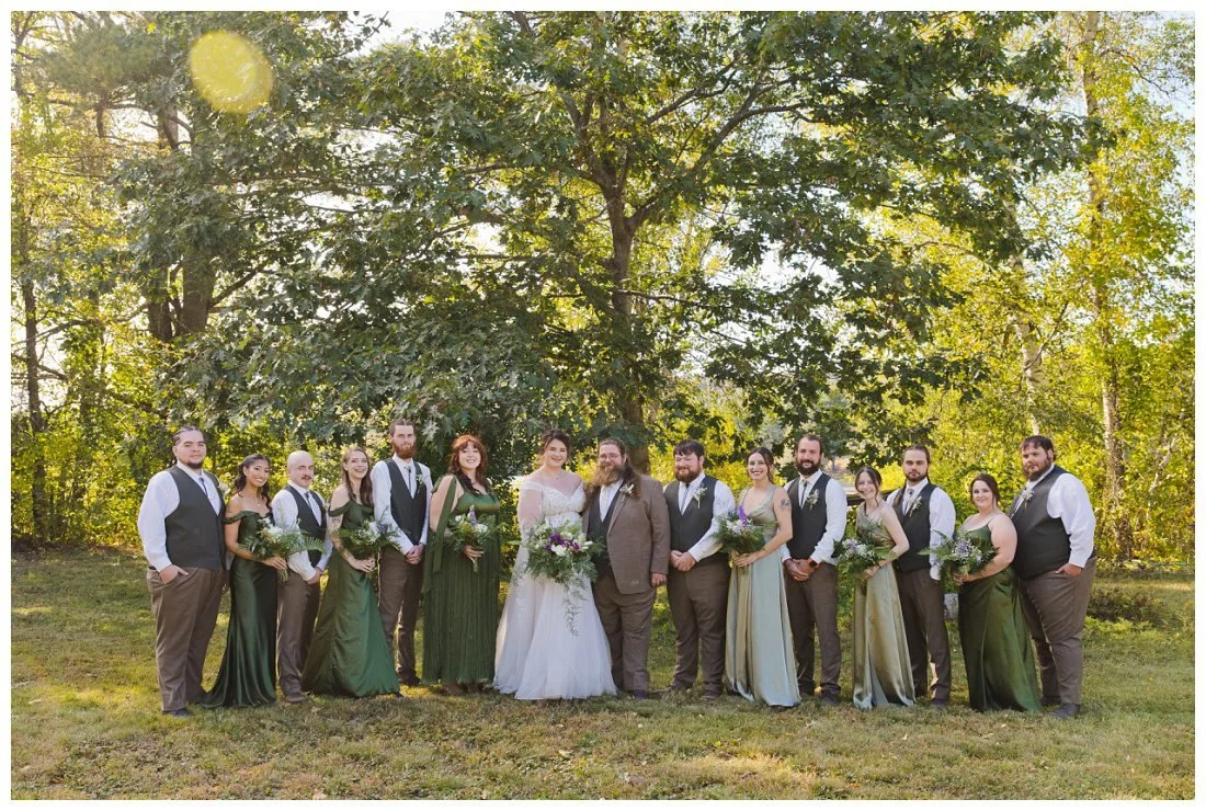 large wedding party with bridesmaids in shades of green and groomsmen in vests and bolo ties