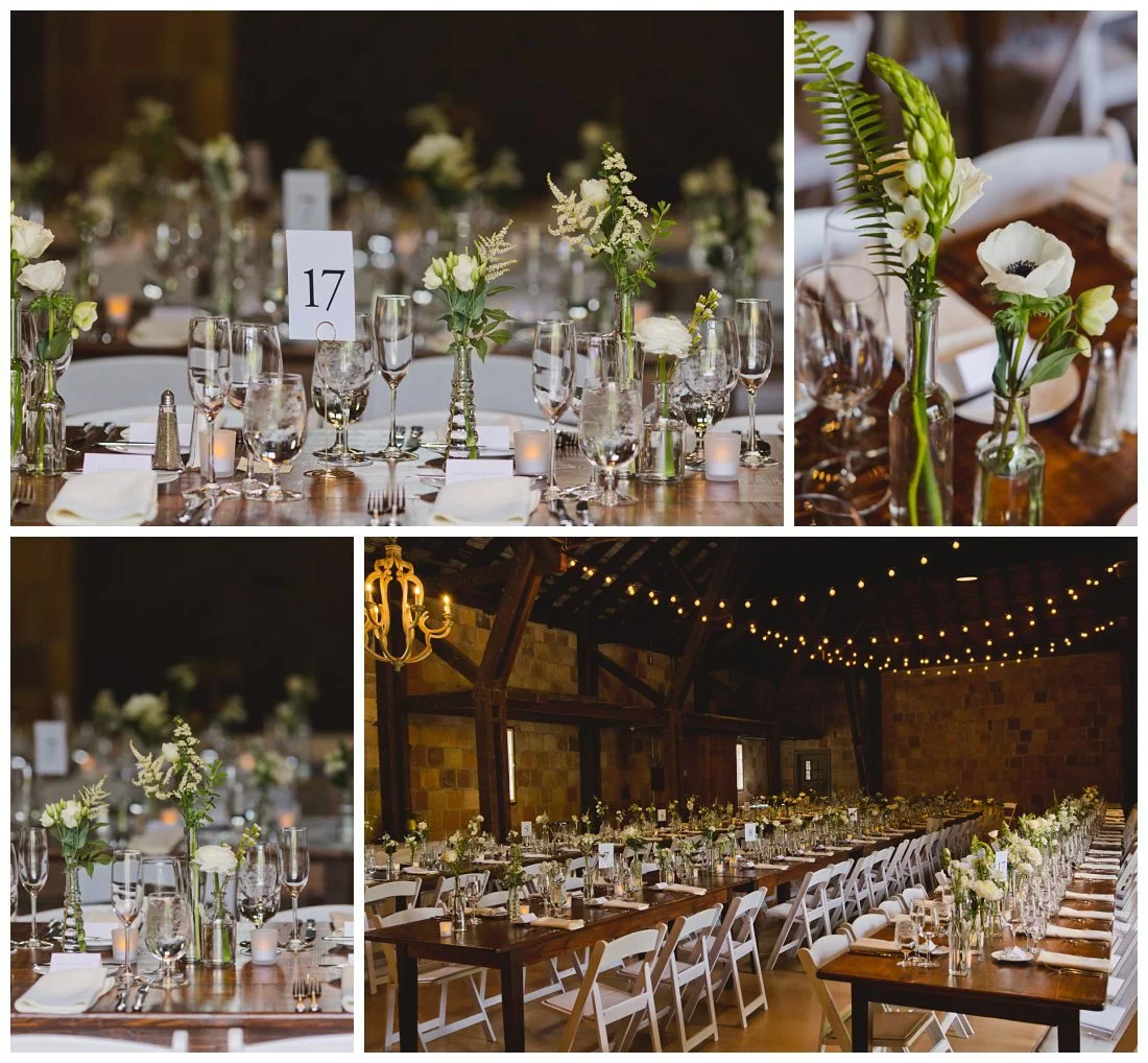 classic and elegant wedding details inside of the barn at crane estate, with bud vases villed with white florals, cafe lights and beautiful italian barn