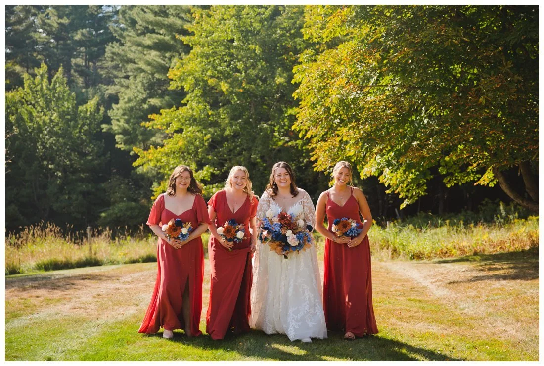 bride and her bridesmaids walk across grassy field with sun shining behind them
