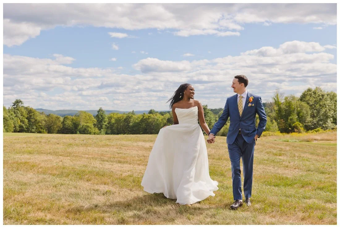 bride and groom walk through field at dell lea with mountains in the background