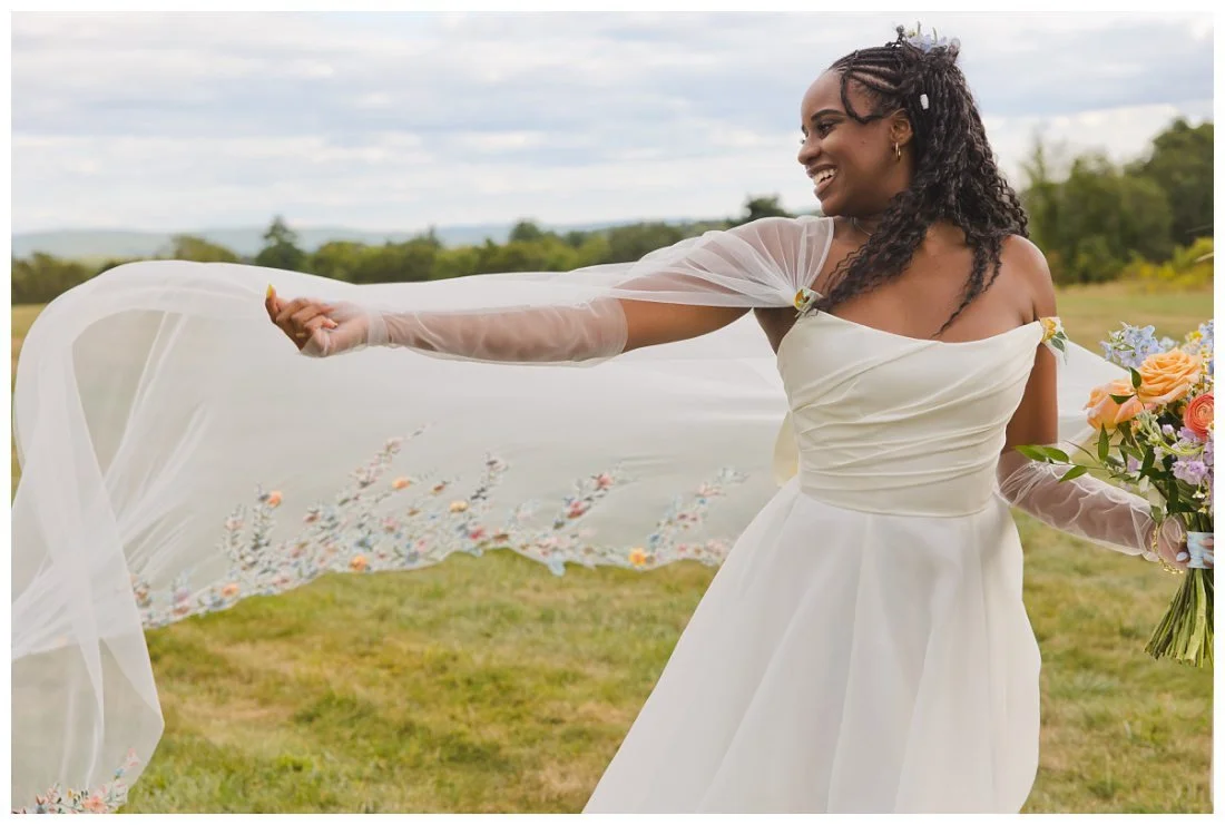bride holds out veil like cape with flower embroidery and it lifts in the wind as she looks back