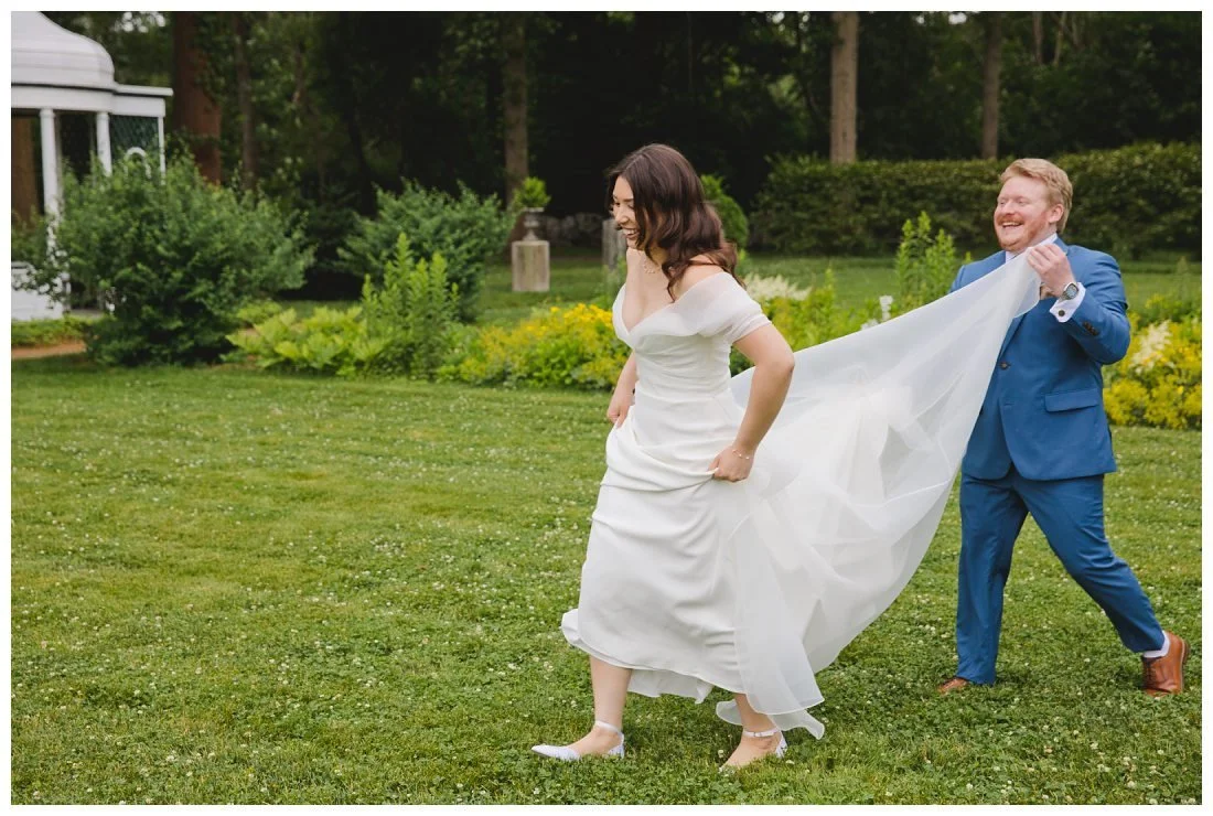 connor helps tara with her dress on the wet lawn on this rainy wedding day
