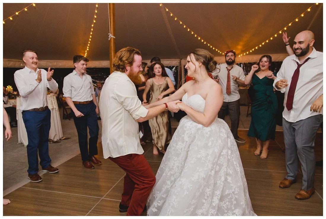 bride and groom hold hands and dance while surrounded by their guests on the dance floor