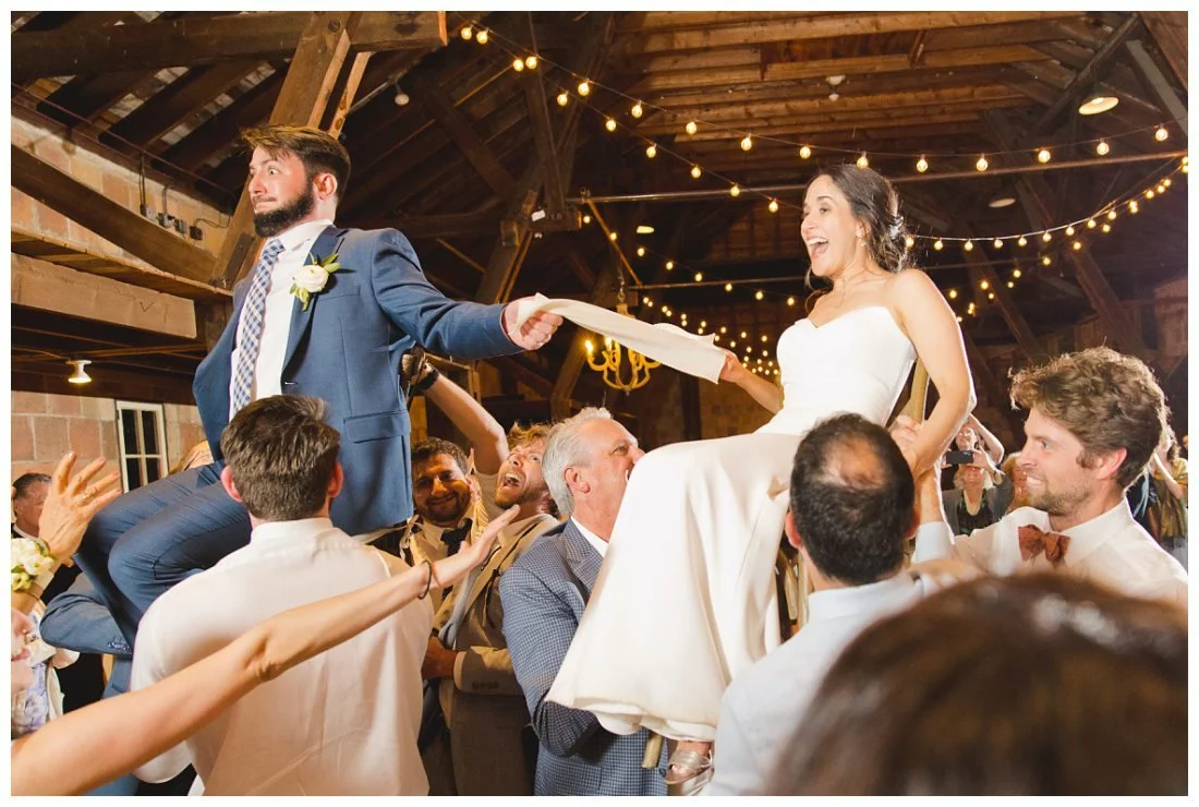 bride and groom get lifted on chairs during the hora and they have funny expressions