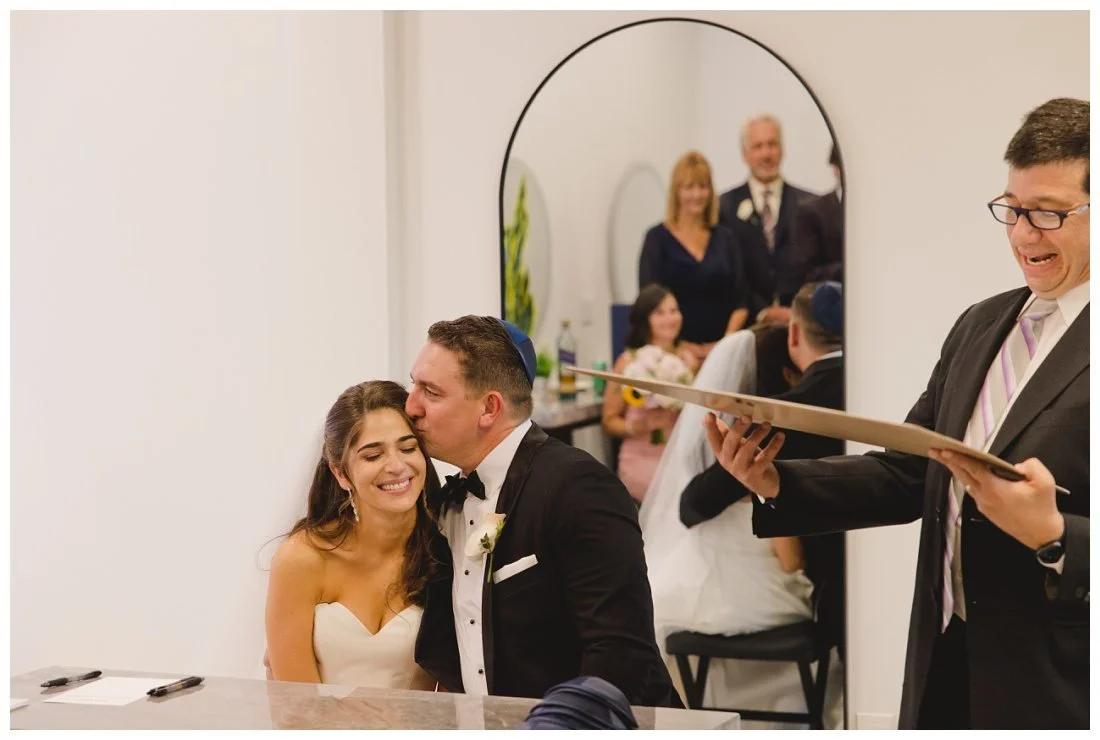 ketubah signing, rabbi reads text while groom gives bride a kiss on the forehead