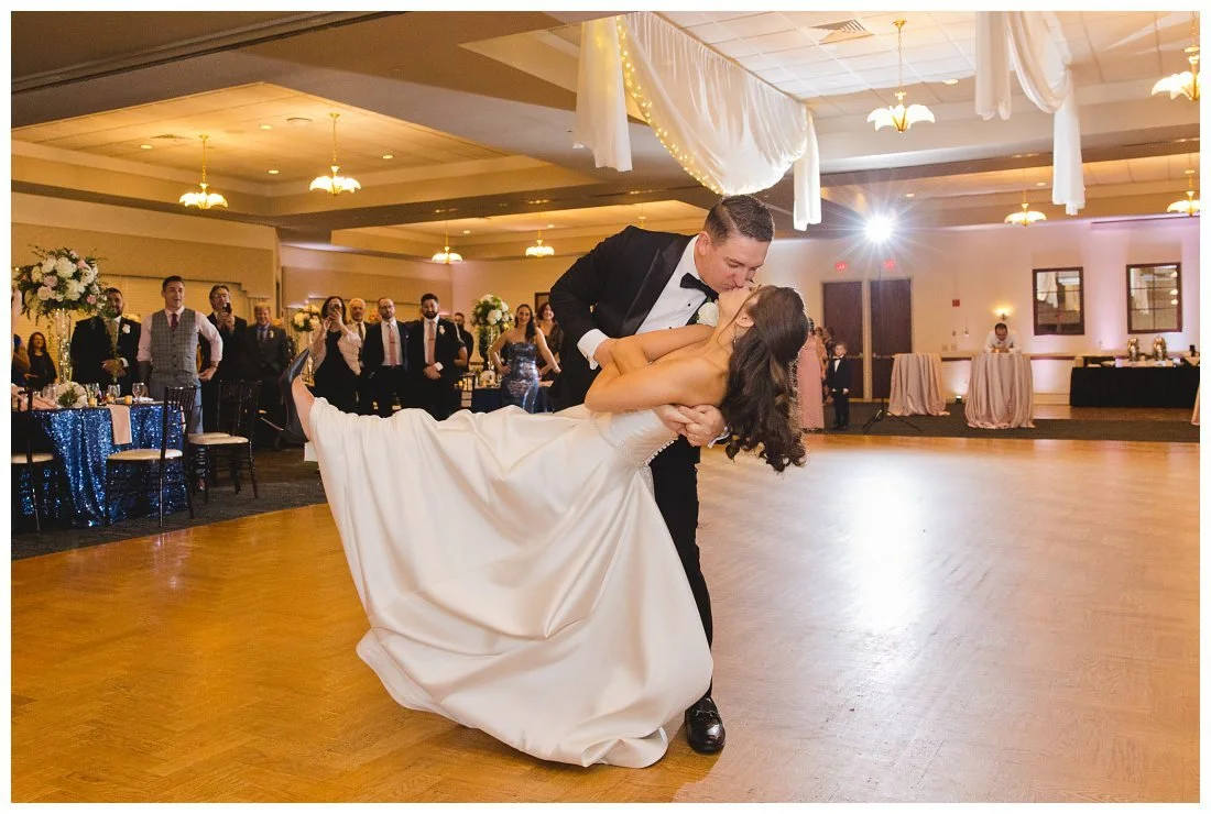 groom dips bride and they kiss with guests behind them during first dance