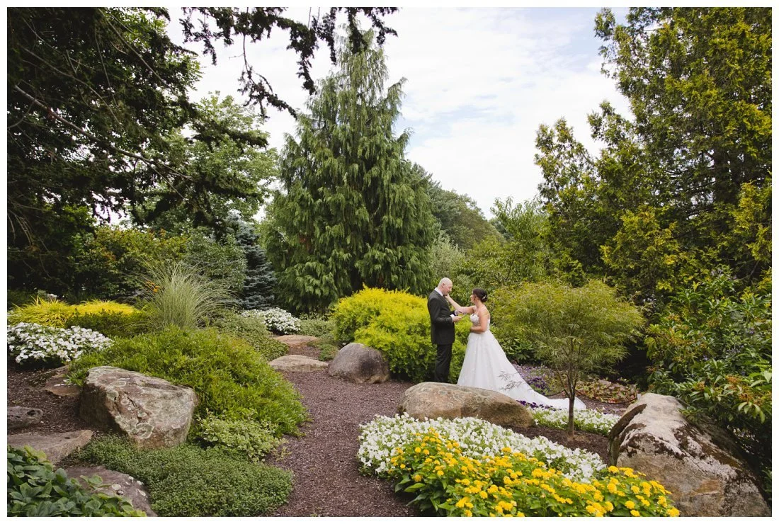 bride reaches out to touch groom's cheek as he reads his private vows to her in this beautiful garden