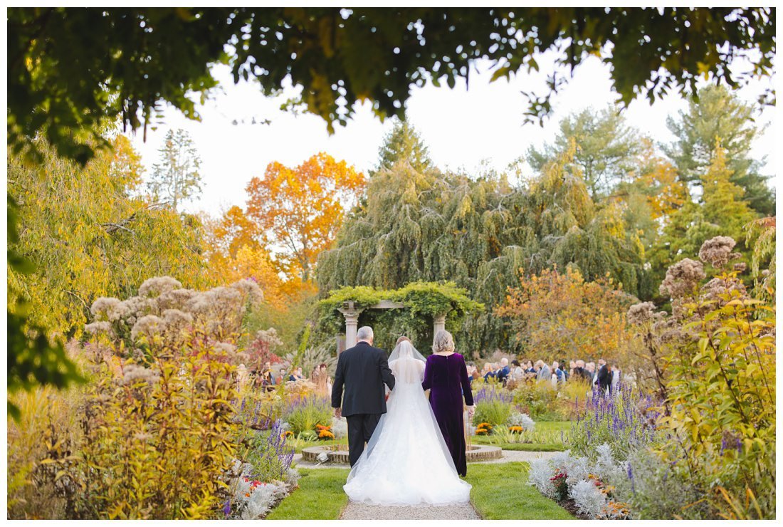 photo of bride with her parents escorting her down the aisle for wedding ceremony, shot from behind with wide angle of the scenery