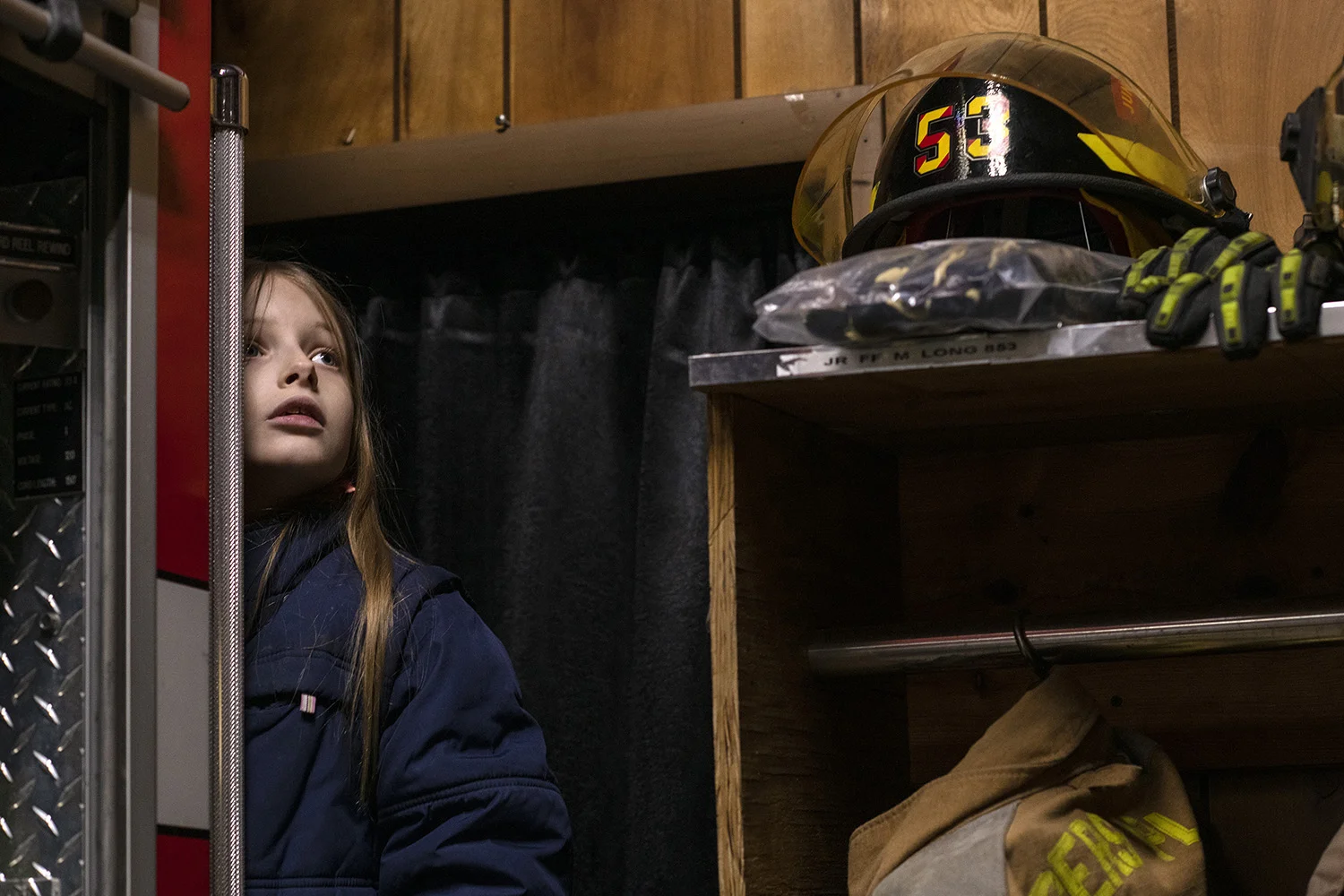  Nevada Johnson, 9, of Tuppers Plains, looks out from behind a firetruck at pictures of firefighters on the adjacent wall inside the Tuppers Plains Volunteer Fire Department. Both Johnson's mother and father are volunteer firefighters with TPFD, and 