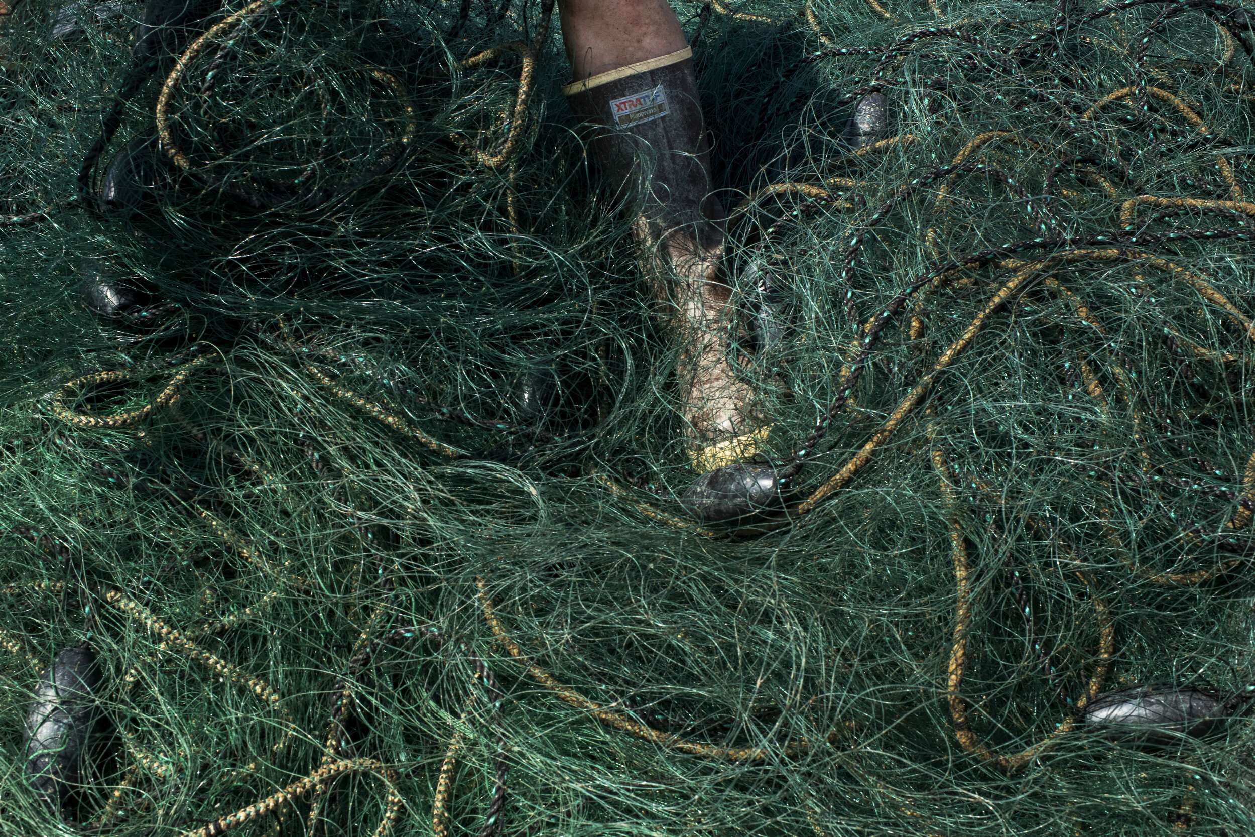 A boot sticks out of a tangled mess of fishing net on the back of a truck as the crew of the DAWN-T remove an old net to be replaced with a new one. Each net, line, cage and countless other products are regulated for their build and quality in order