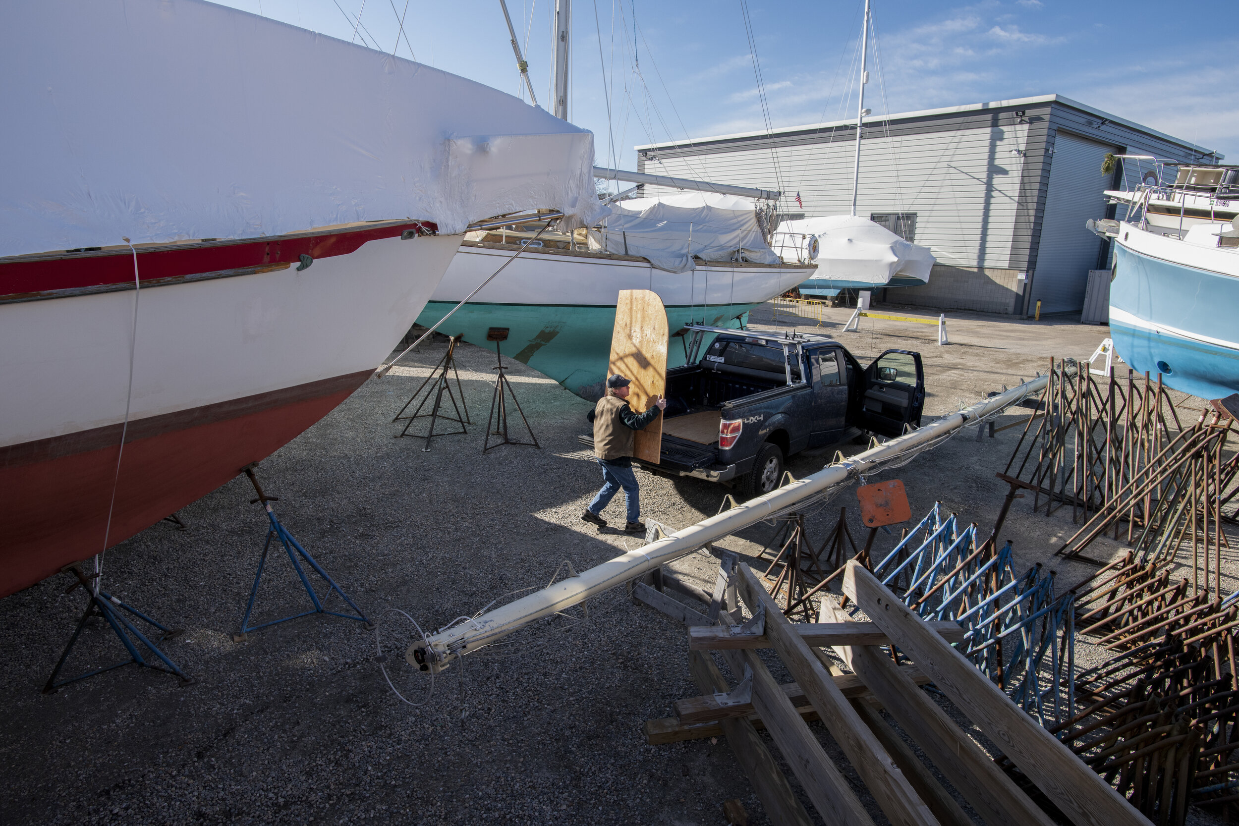 Tim Barrett carries a piece of wood to be used as deck replacement while working in the boat yard on Christmas Eve. With low quotas and low market prices, Barrett finds work on land more financially rewarding than fishing in the winter. Repairing bo