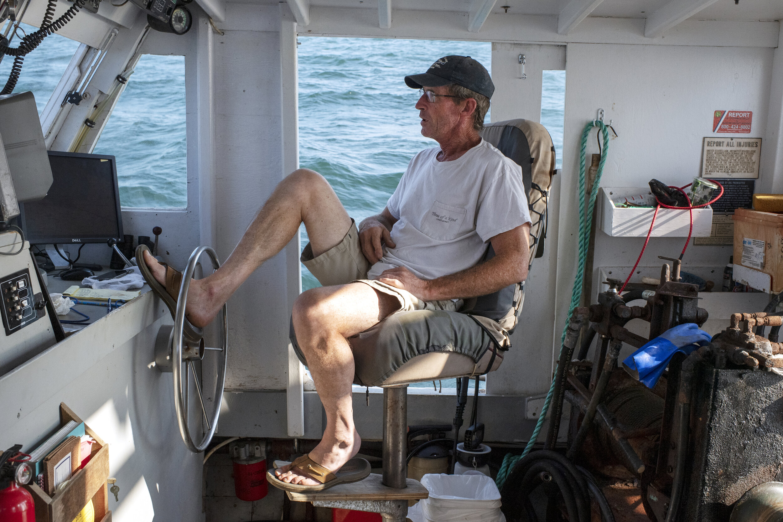 Fisherman Tim Barrett steers his fishing boat, Odessa, with his foot while trawling the waters near Nantucket Sound for conch and flounder. Fishing has an allure to outsiders that fishermen like Barrett will acknowledge, joking that few who try will