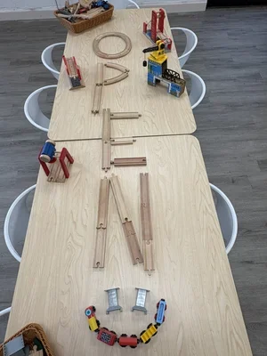 Wooden train tracks arranged on a table to spell the word 'OPEN'. Toy trains and accessories are placed around the tracks.
