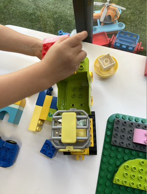 Child assembling colorful Lego bricks on a white table, with Lego vehicles and parts nearby.