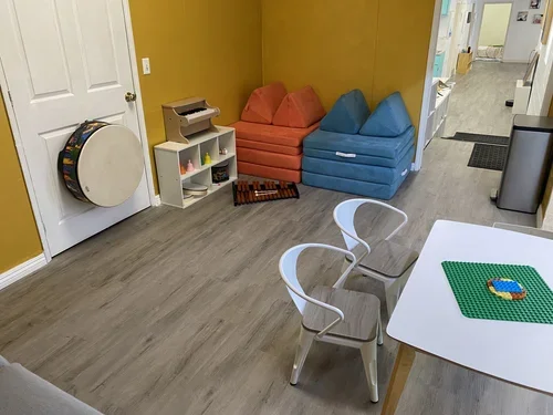 Playroom with colorful block chairs, small table with Lego pieces, and musical instruments on the wall.