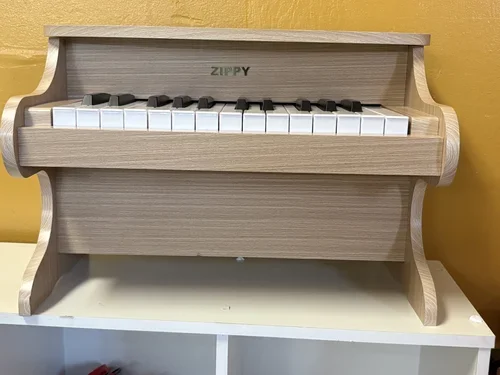 Small wooden toy piano with black and white keys, placed on a shelf against a yellow wall.