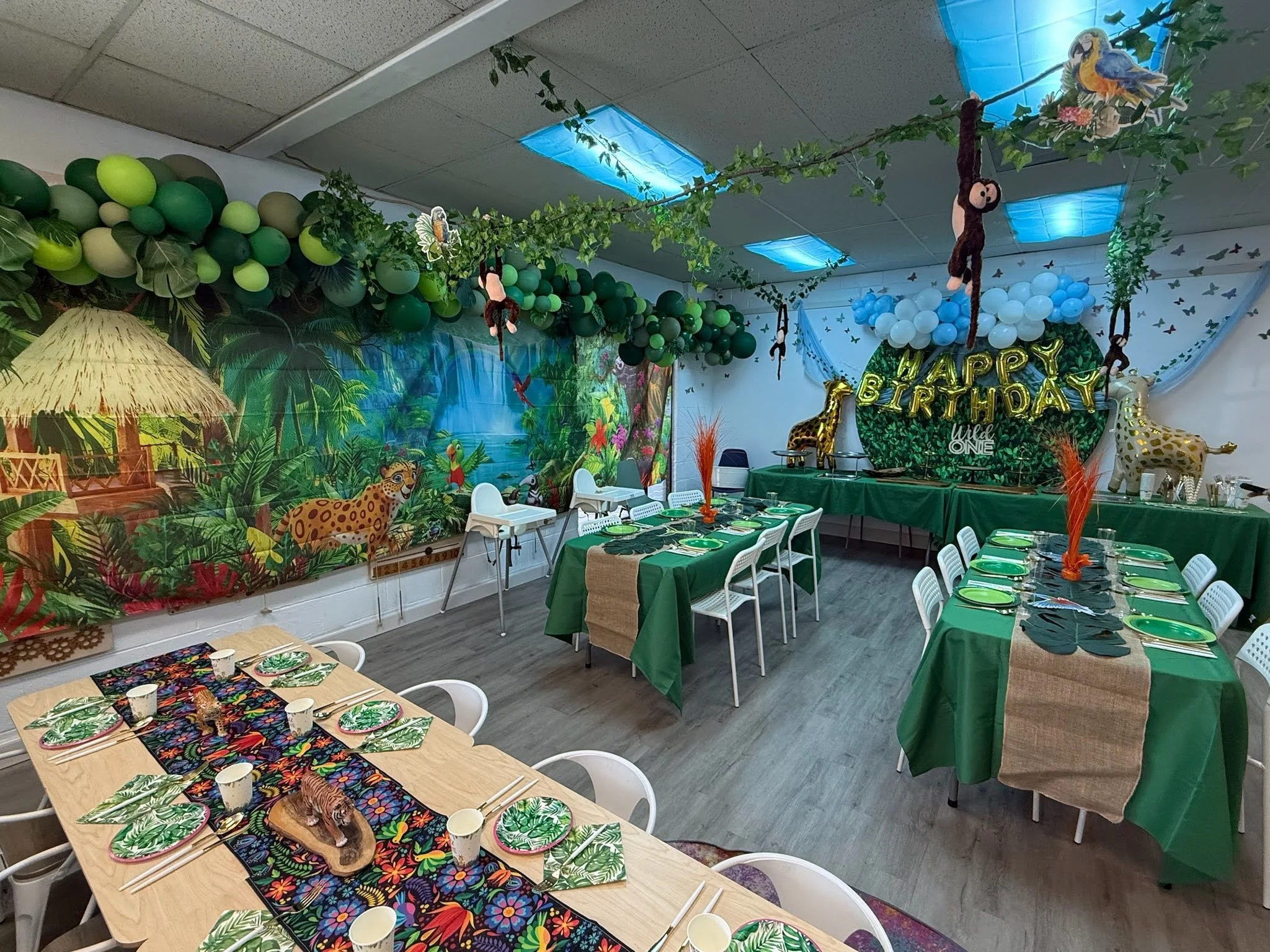 Full room view of a jungle-themed birthday party at PlayLab Hollywood with jungle mural, table settings, and balloon decor
