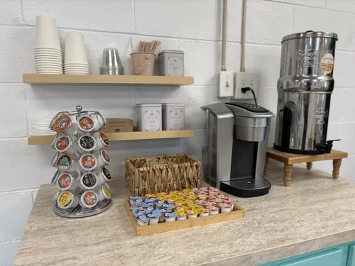 Coffee station with disposable cups, coffee pods, a Keurig machine, and a water dispenser on a countertop.