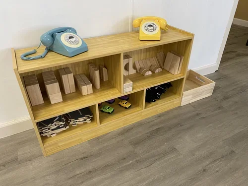 Wooden shelves with toy wooden blocks, toy cars, and train tracks, topped with two vintage rotary dial toy phones, one blue and one yellow.