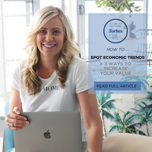 A smiling woman with blonde hair holding a silver Apple MacBook laptop, sitting in a bright room with plants and patterned wallpaper, alongside a blue and white poster promoting Forbes Coaches Council and economic trends.