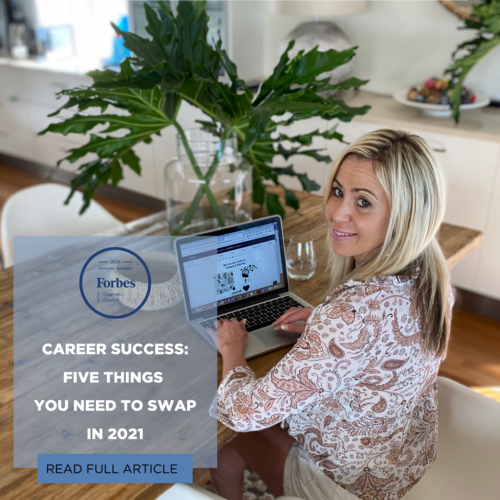 A smiling woman with blonde hair working on a laptop at a wooden table in a bright room, with a large leafy green plant in a glass vase nearby.
