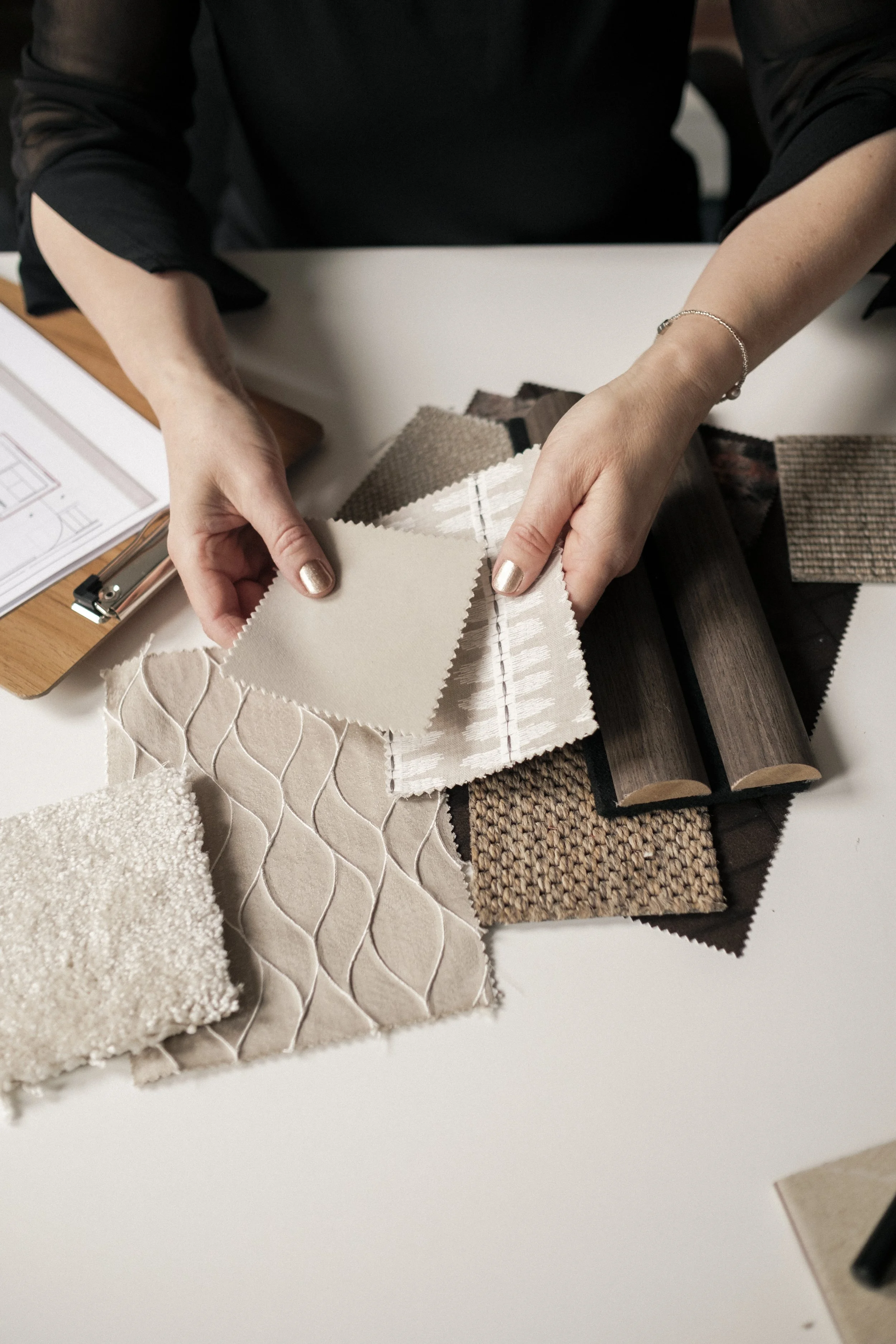 A person showing various fabric swatches and textured samples on a table, with a blueprint and design tools nearby.
