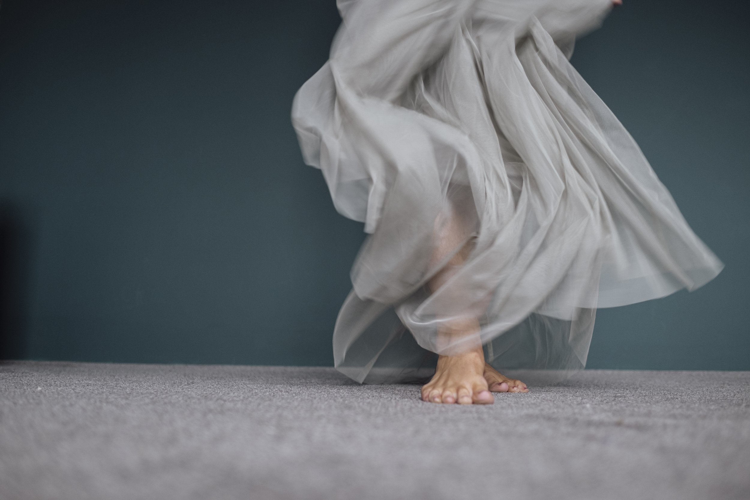 Person in a flowing gray dress balancing on their hands on a gray carpeted floor.