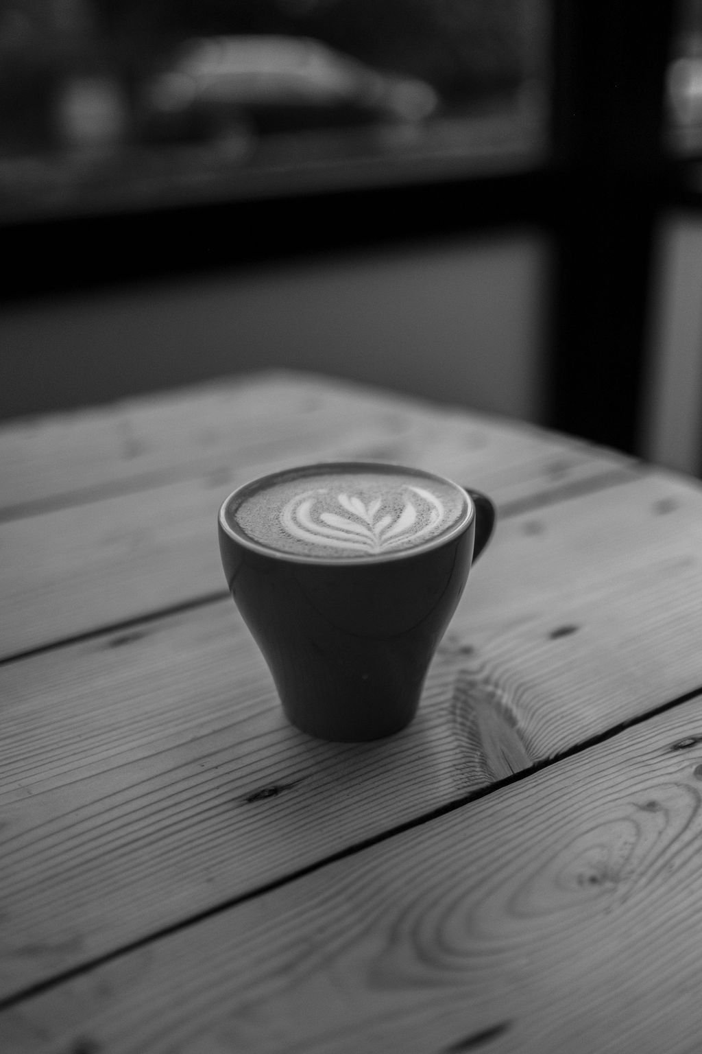 Black coffee cup with latte art on a wooden table in a café setting.