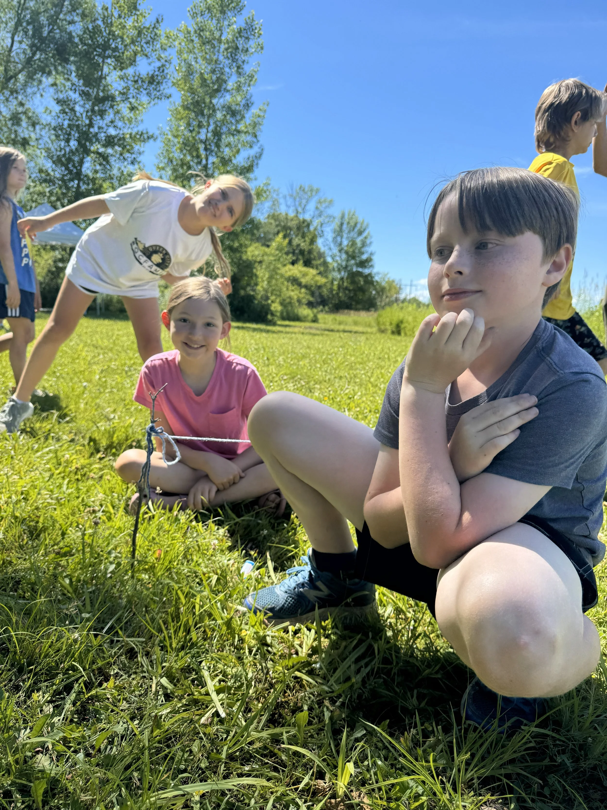 3 campers sitting on a grassy field, smiling at the camera