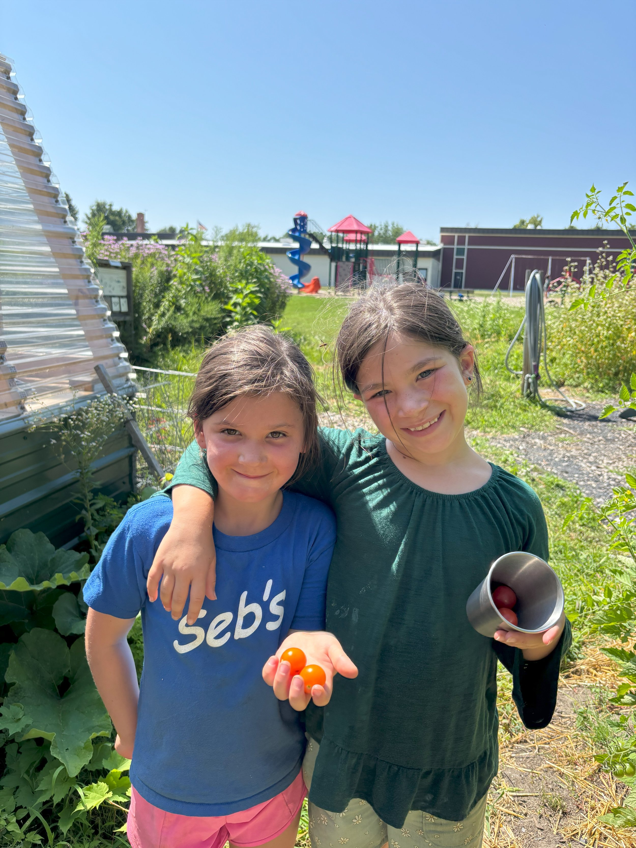 Two summer campers smiling and holding their freshly harvested cherry tomatoes in the garden