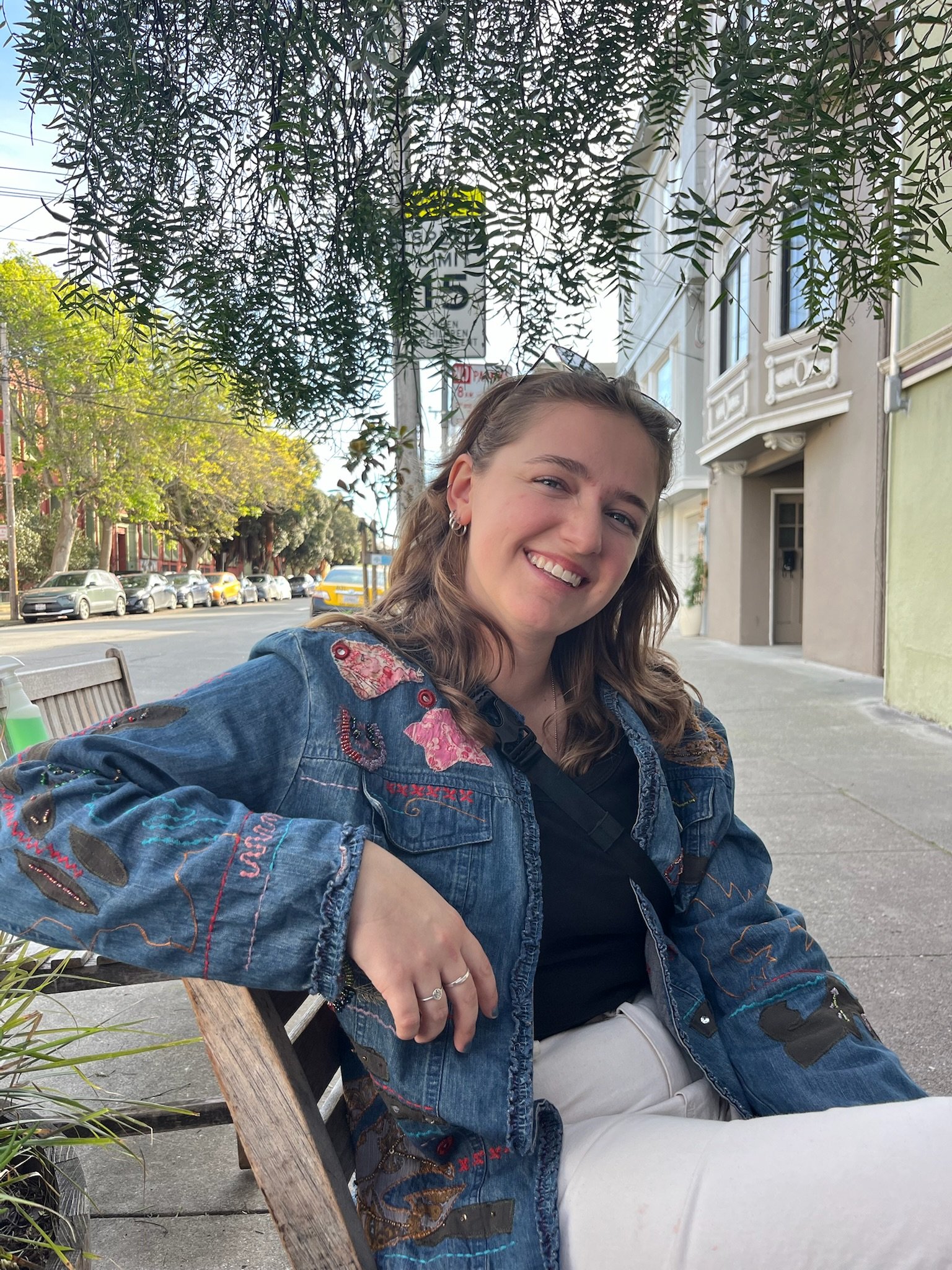 bio photo of Emily sitting on a bench along a street, smiling at the camera