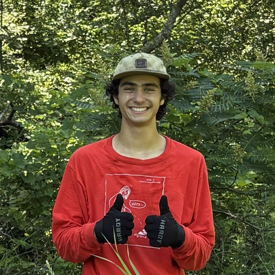 Max at a volunteer work party, smiling at the camera with both thumbs up