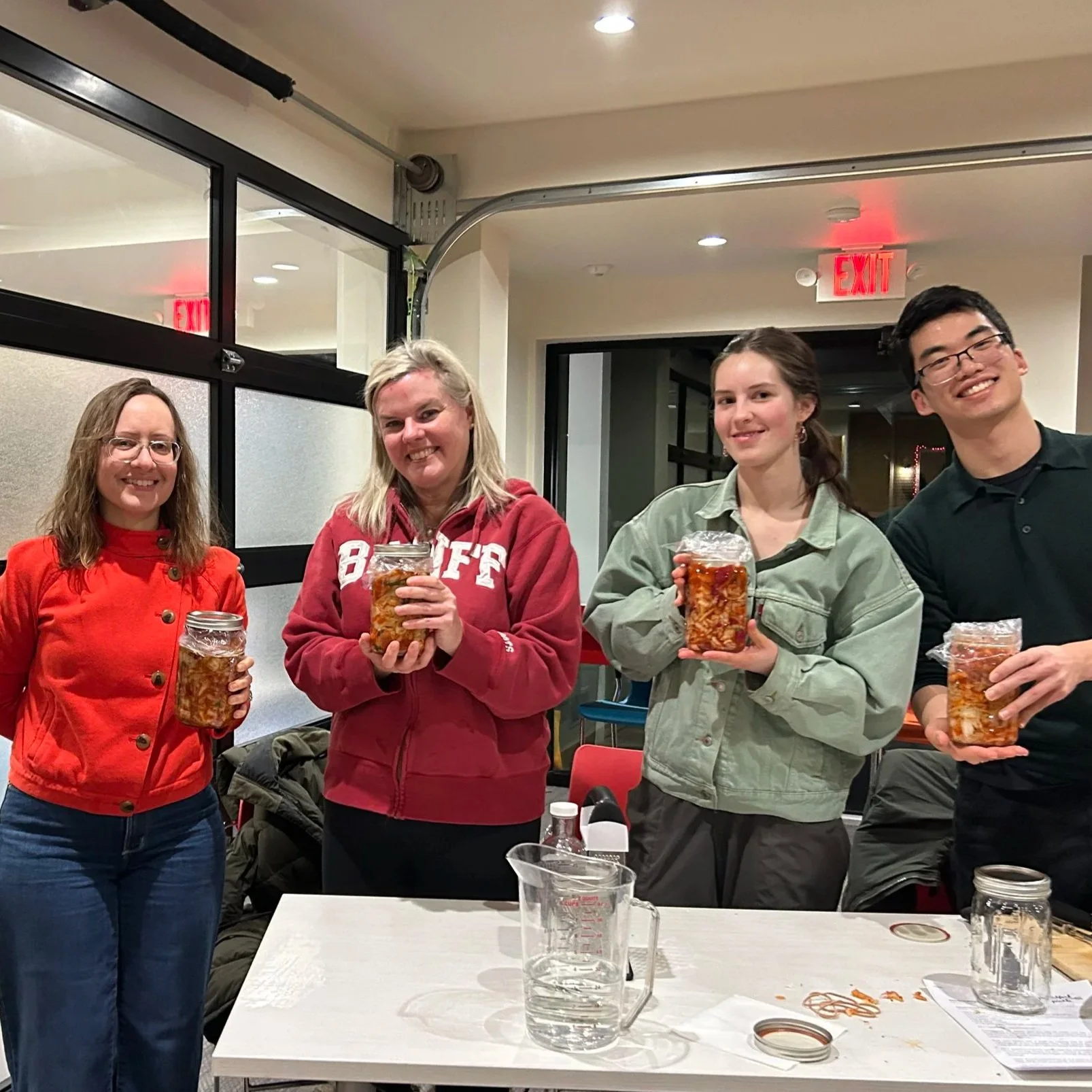 4 adults standing around a table, showing off their finished kimchi