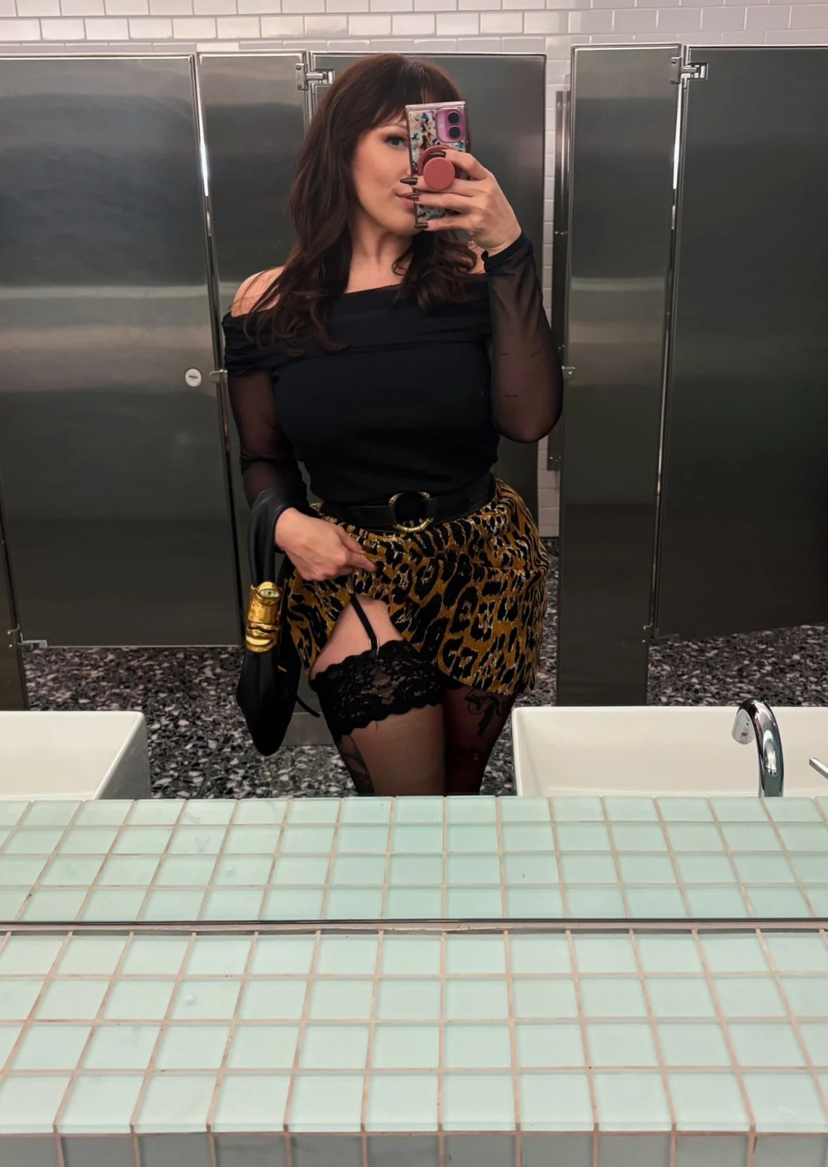 Zoey Belladonna in a bathroom selfie lifting up her leopard print skirt to expose her garter belt holding up her black nylon stockings.