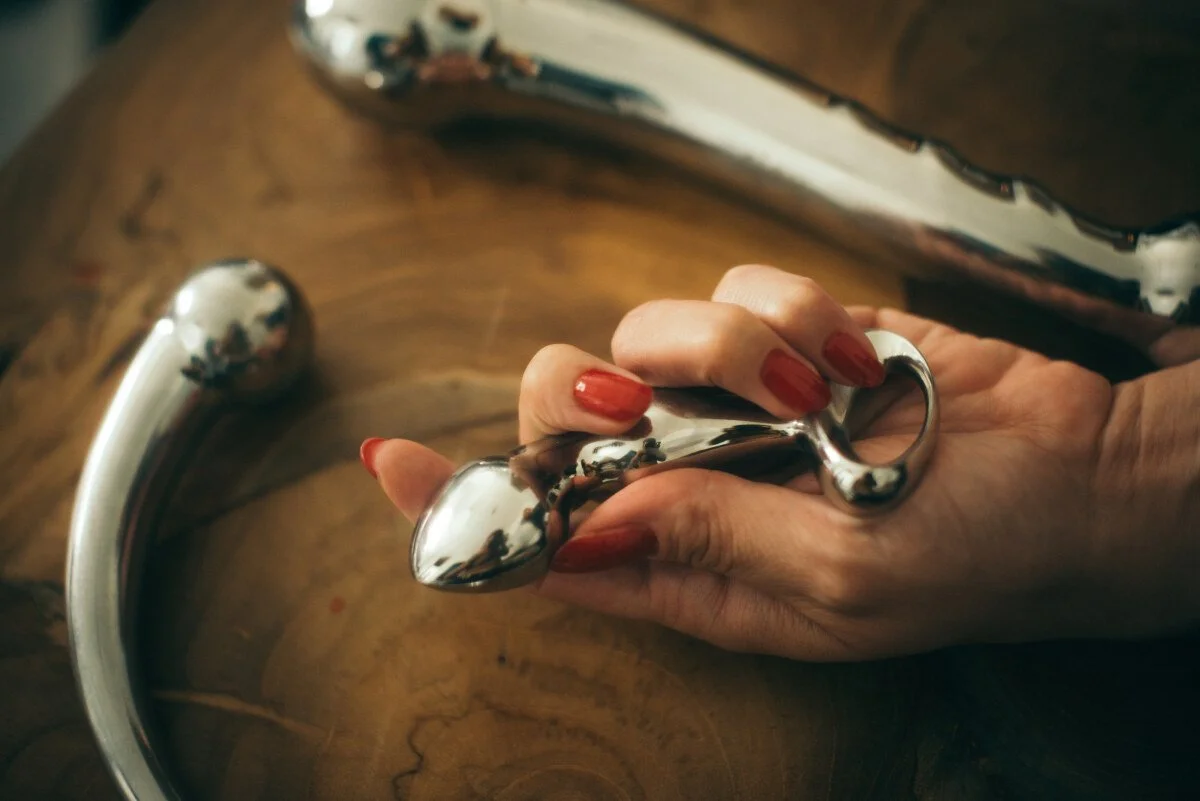 A person with red painted nails holds a shiny metallic object, they are massage wands.