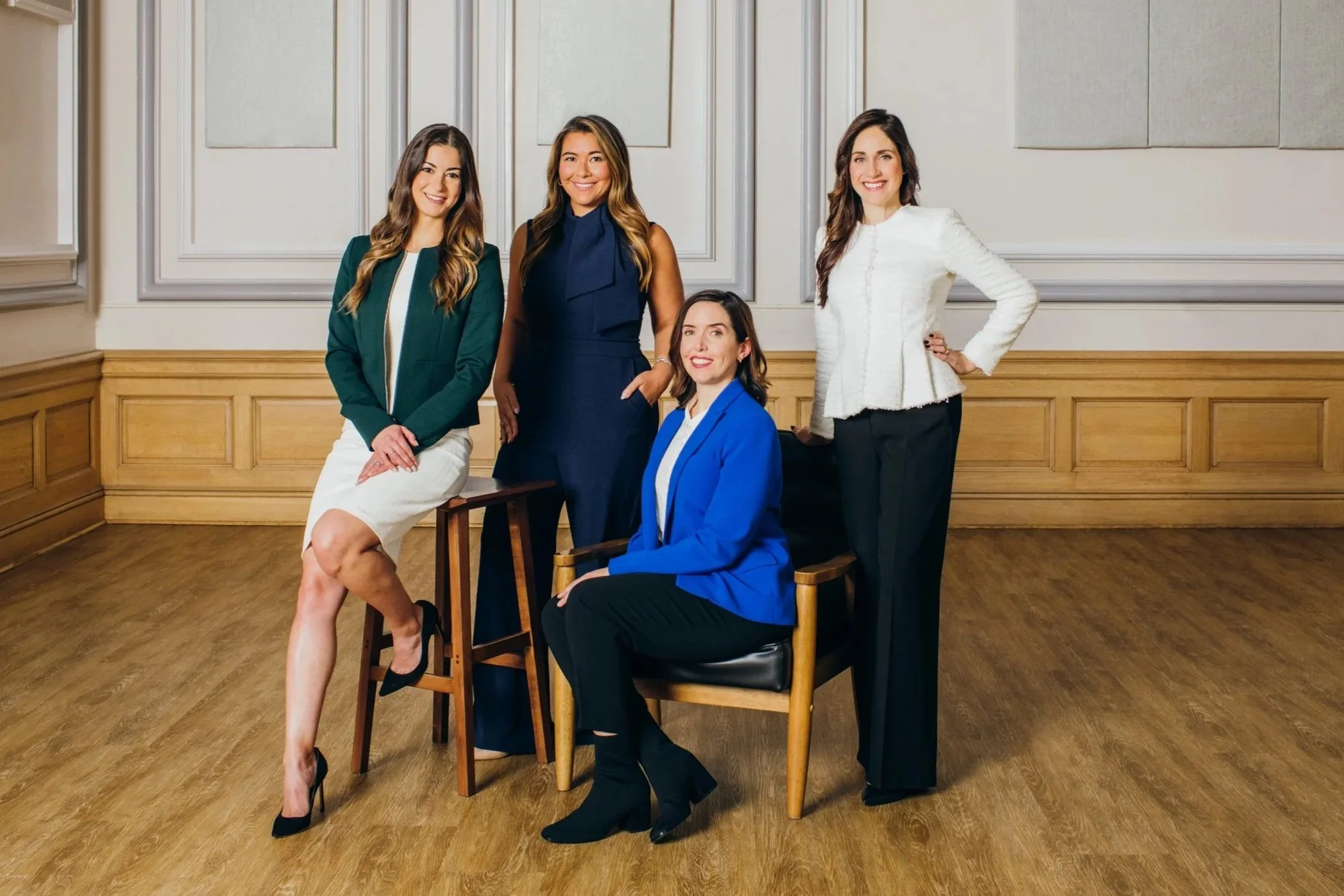  Portrait of 4 women attorneys in a beautiful old federal courthouse.  Some are sitting, some are standing &amp; they are dressed in modern business attire. 